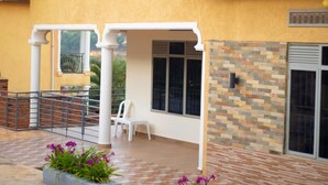 A covered outdoor area with a brick floor, a white railing, and a seating area with a chair. - Inviting 6-bedrooms Apartment in Kigali (Kigali)