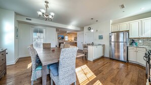 A spacious kitchen with white cabinets, a stainless steel refrigerator, and a dining area with wicker chairs and a wooden table.