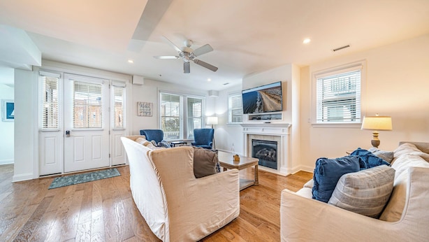 A spacious living room with a fireplace, a television mounted above it, and a ceiling fan.