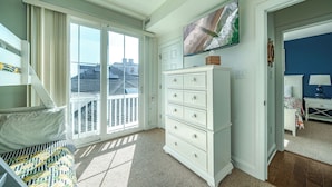 A bedroom with a bed, a dresser, a TV, and a view of the city through large windows.