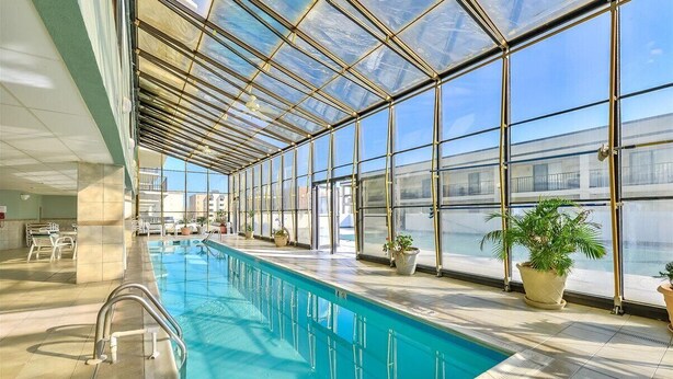 Une piscine intérieure dotée d’un toit en verre, de plantes en pot et d’un sol carrelé.