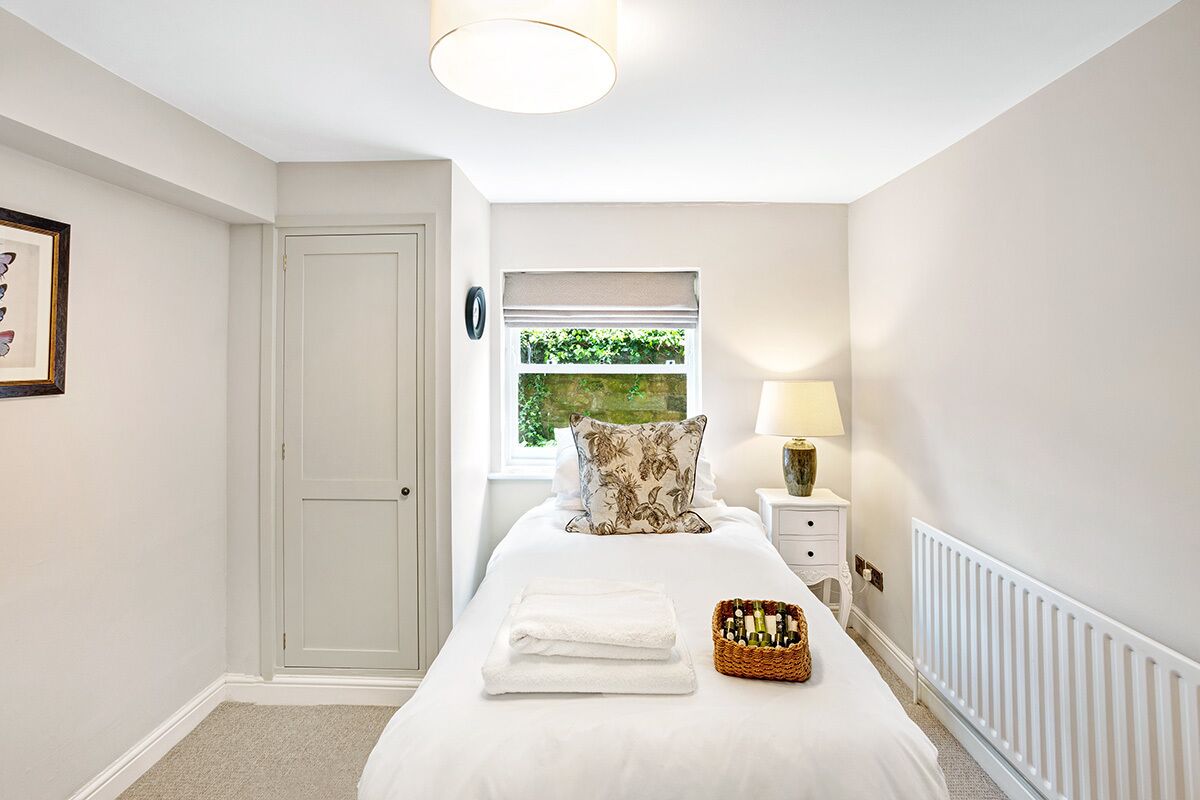 A bedroom with a bed, a nightstand, a lamp, a window with a view of greenery, and a door.