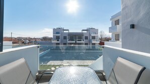 Ein Balkon mit Glastrennwand, zwei Stühlen und Blick auf ein modernes Gebäude mit Balkonen.