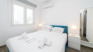 Ein ordentlich bezogenes Bett mit weißen Leinen und Handtüchern, ein blauer Kopfteil, Nachttischlampen und ein großer Spiegel an der Wand.