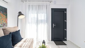 Ein modernes Wohnzimmer mit Sofa, Lampe, Tür und Fenster mit leichtem Vorhang.