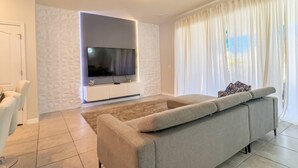 A modern living room with a large flat-screen TV, a beige sofa, and a patterned wall.