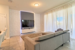 Un salon moderne doté d’un grand téléviseur à écran plat, d’un canapé beige et d’un mur orné d’un motif.