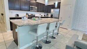 A modern kitchen with dark cabinets, a granite countertop, stainless steel appliances, and bar stools.