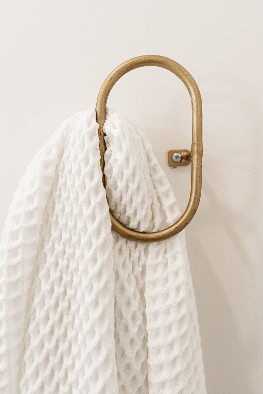 Een wit, gestructureerd doek hangt aan een koperen ring aan de muur.