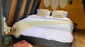A cozy, wooden-framed attic bedroom with a large bed, a small table with candles, and a window with a view of greenery. - Unique Lake House breathtaking views (Guatape)