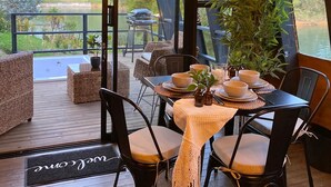 A dining area with wicker furniture, a table set for four, and a view of a lake and hills. - Unique Lake House breathtaking views (Guatape)