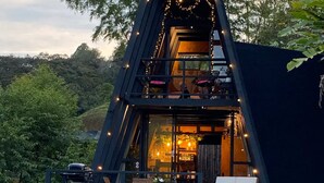 A two-story wooden structure with a balcony, string lights, and a view of the surrounding greenery. - Unique Lake House breathtaking views (Guatape)