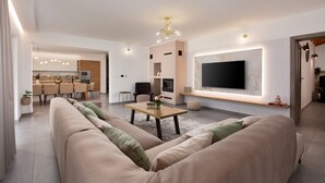 A modern living room with a large sofa, a coffee table, and a flat-screen TV mounted on the wall. - Charming Villa Filton with swimming pool, sauna and jacuzzi (Markovici)
