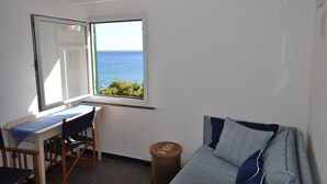 A room with a view of the sea, a desk with a chair, a sofa, and a small round stool. - Virginia House - CITRA 011019-LT-0354 (Monterosso al Mare)