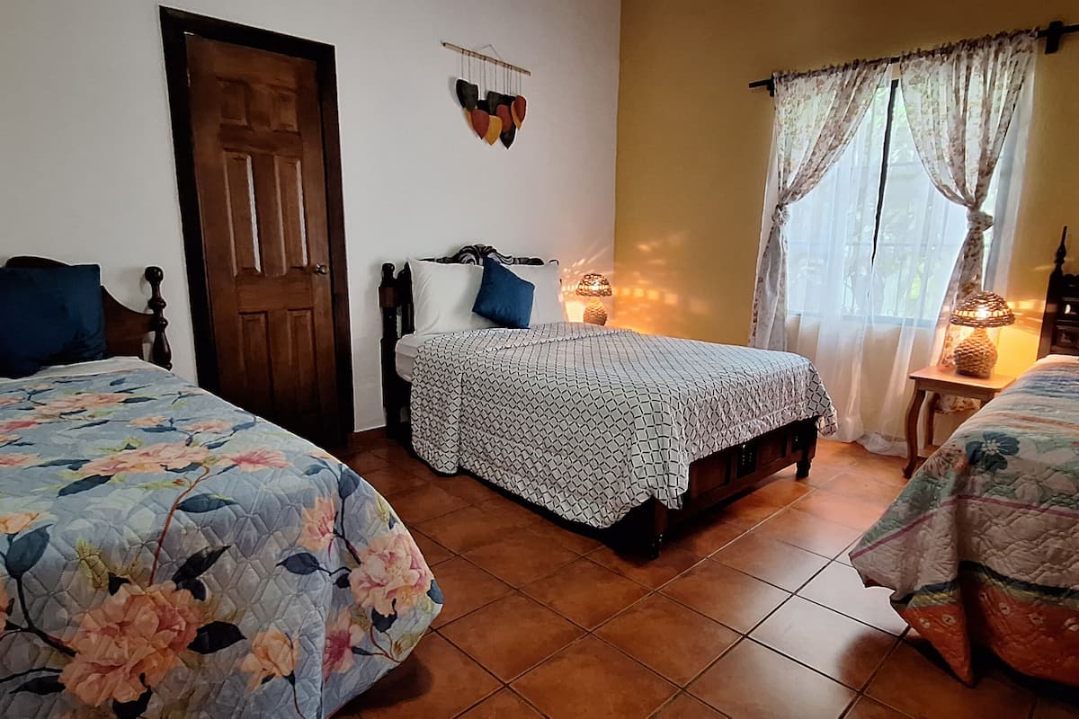 Una habitación con tres camas, una puerta de madera, un adorno en la pared y una ventana con cortinas.