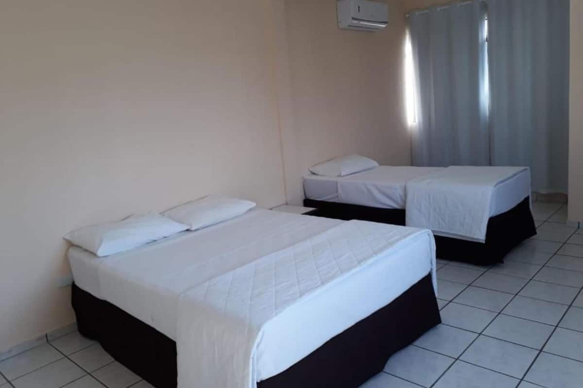 A hotel room with two beds, white bedding, a tiled floor, and a window with curtains.