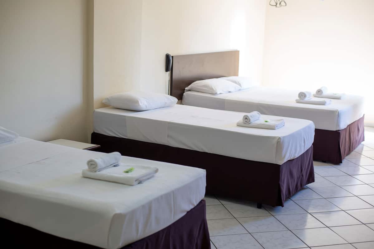 A hotel room with three single beds, each with a pillow and a rolled towel.