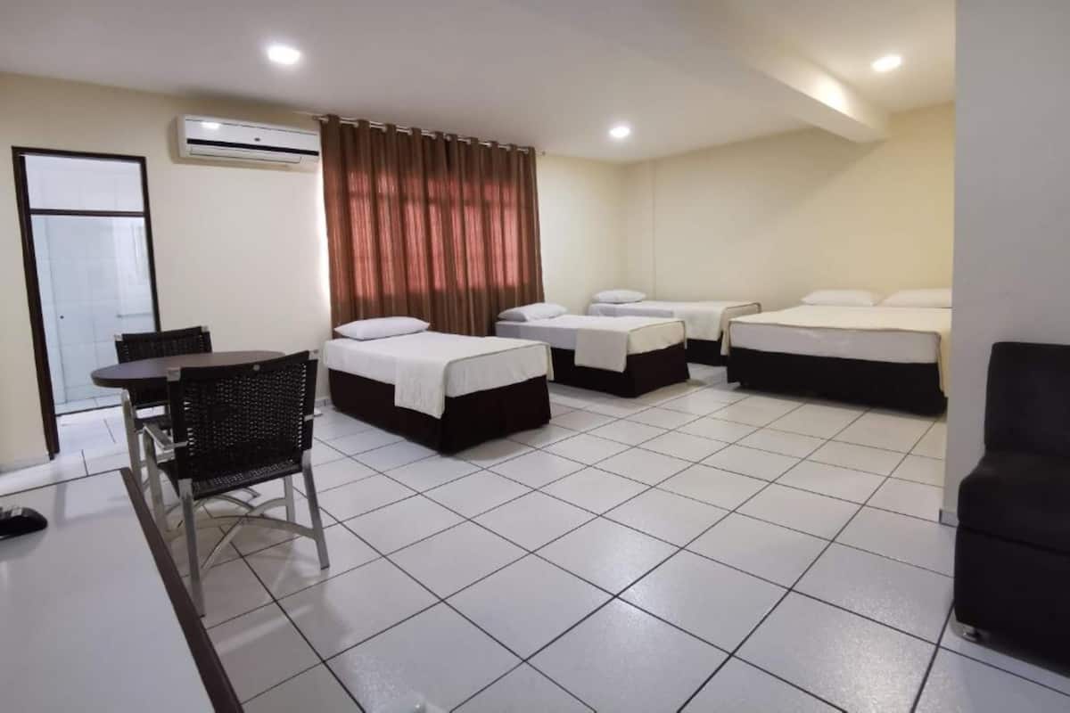 A hotel room with two single beds, a small table with a chair, and an air conditioning unit on the wall.