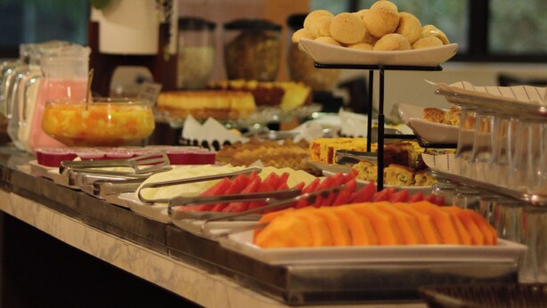 A buffet with various food items, a flower vase, and a window in the background. - Smart Cataratas Hotel (Foz do Iguaçu)