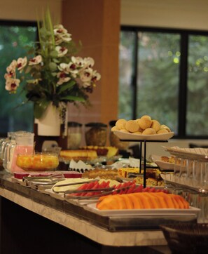 A buffet with various food items, a flower vase, and a window in the background.