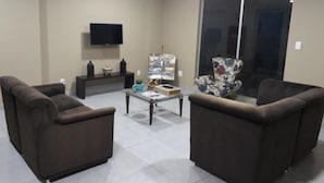 A living room with two brown sofas, a glass coffee table, a flat-screen TV mounted on the wall, and a decorative cabinet. - Smart Cataratas Hotel (Foz do Iguaçu)