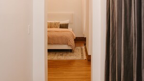 A narrow hallway with wooden flooring leading to a bedroom with a bed and curtains. - Oregon District Oasis - The Best of Downtown (Dayton)
