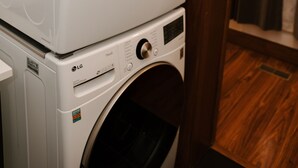 A stacked washer and dryer unit in a room with wooden flooring and a door with a curtain. - Oregon District Oasis - The Best of Downtown (Dayton)