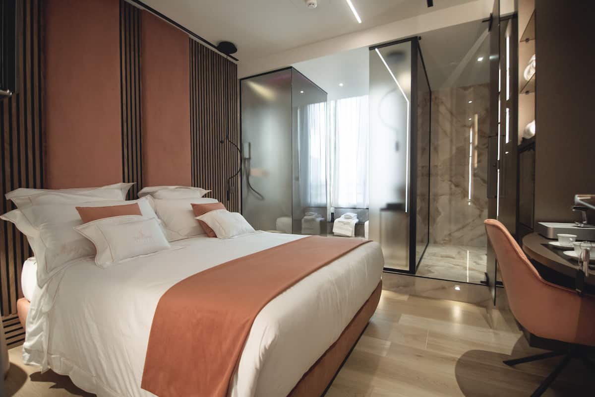 A modern hotel room with a large bed, a desk, and a bathroom with a glass shower.