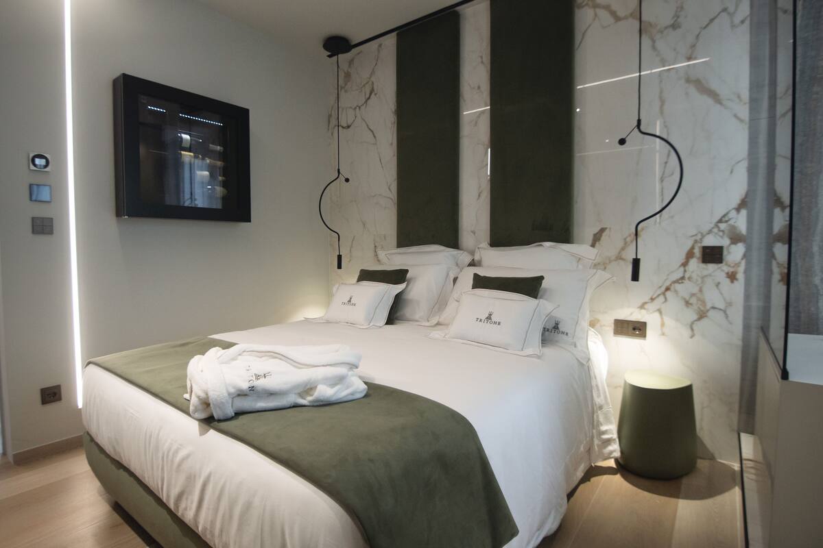 A modern hotel room with a large bed, a flat-screen TV mounted on the wall, and a marble-patterned wall.