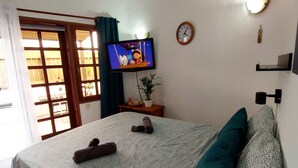 A bedroom with a bed, pillows, a television, a clock, and a plant.