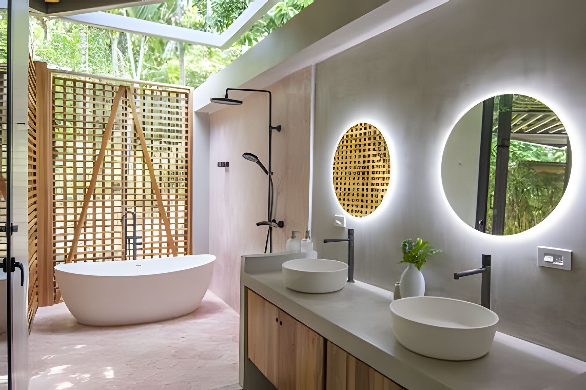 Une salle de bain moderne avec une baignoire sur pieds, deux vasques et un grand miroir agrémenté d’un luminaire circulaire.