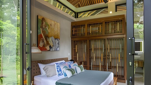 A bedroom with a bed, a painting, a TV, and a view of the outdoors. - Caribbean Courtyard Villas 6 to 10 pp (Cahuita)