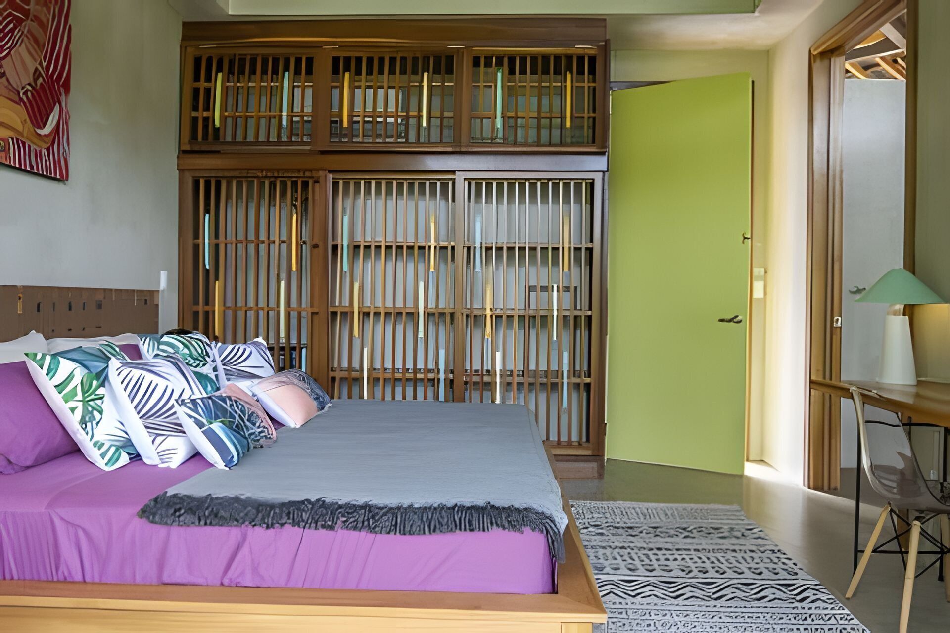 A bedroom with a bed, a wooden headboard, a green door, and a chair with a lamp.