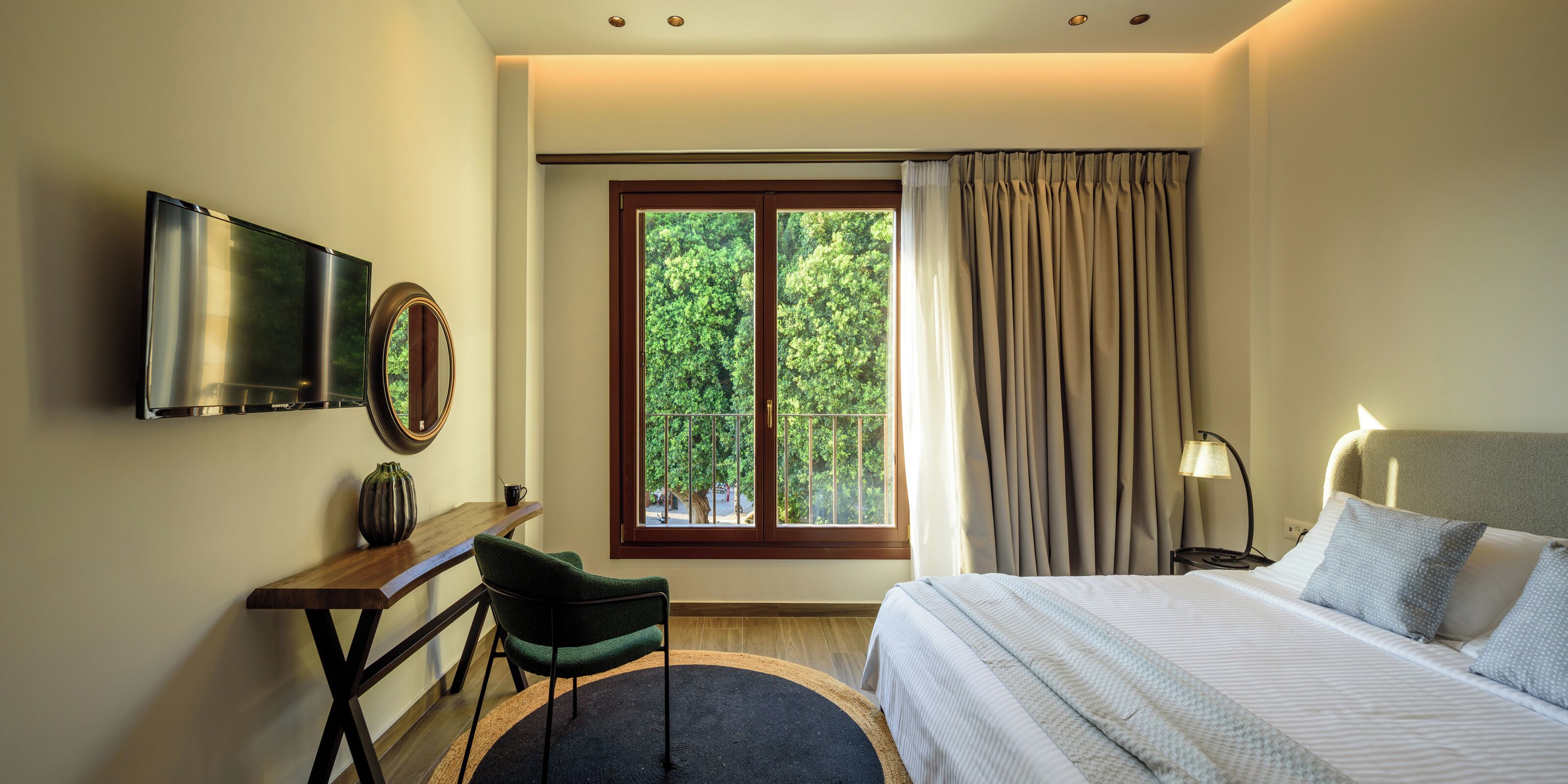 A hotel room with a bed, a desk, a chair, a TV, and a window with curtains.