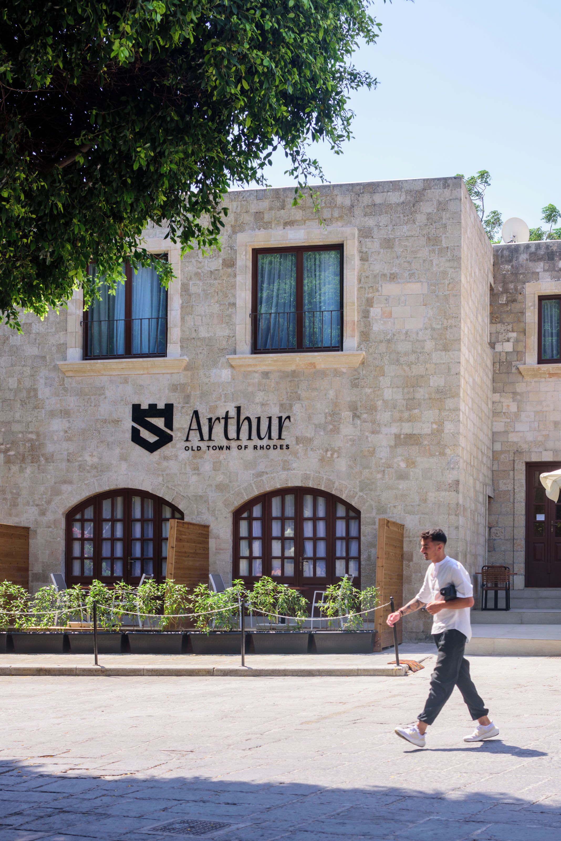 A building with the sign "Arthur Old Town of Rhodes" and a man walking in front.