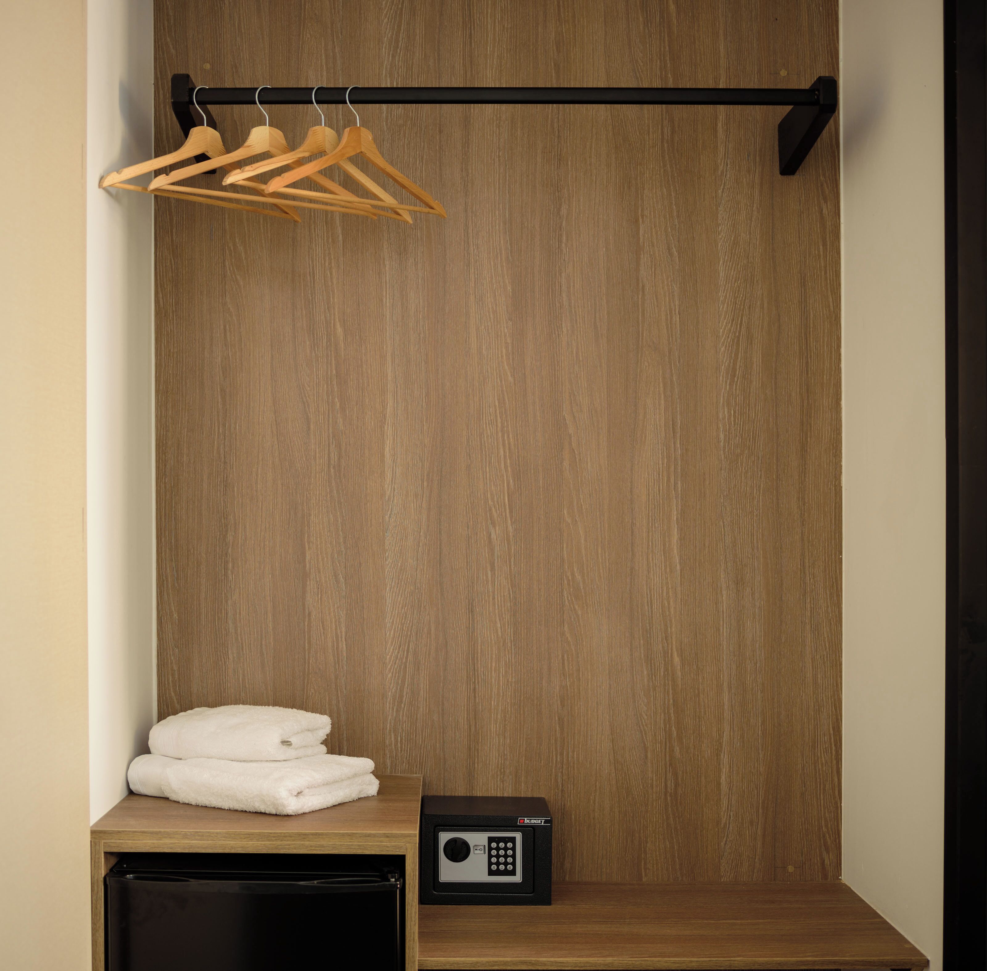 A wooden wardrobe with a hanging rack for clothes and a small table with a radio.