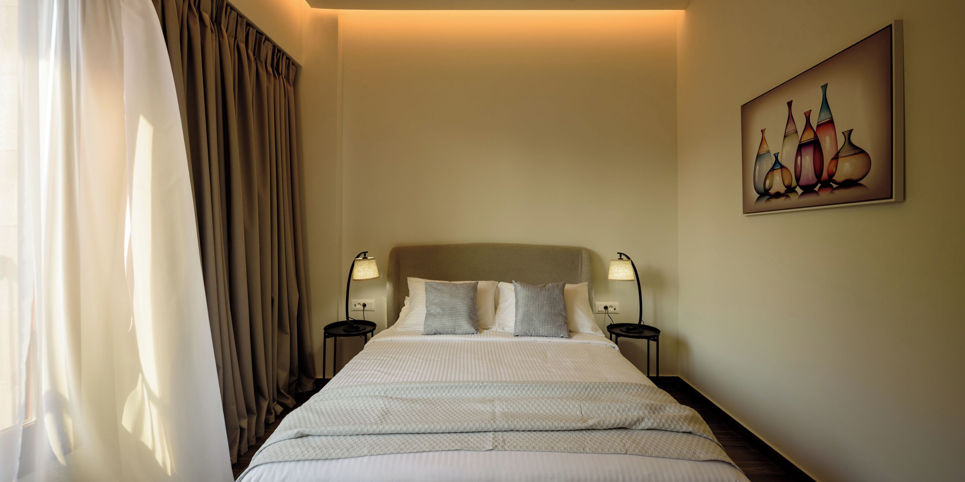 A hotel room with a bed, two bedside tables with lamps, a painting on the wall, and a window with curtains.
