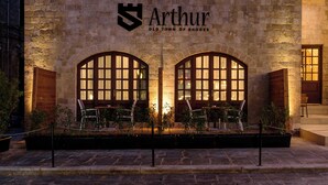 Ein Steinhaus mit der Aufschrift "Arthur Old Town of Rhodes" und zwei Rundbogenfenstern mit Sitzgelegenheiten davor.