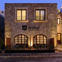 A stone building with the name "Arthur Old Town of Rhodes" and two arched windows with seating in front.
