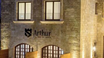 Een gebouw van steen met een bord waarop “Arthur” staat en een logo boven de ingang.