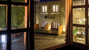 Blick durch ein Fenster eines Gebäudes, das den Namen 'Arthur' an der Fassade trägt, mit Steinmauern, Rundbogenfenstern und Außenplätzen.