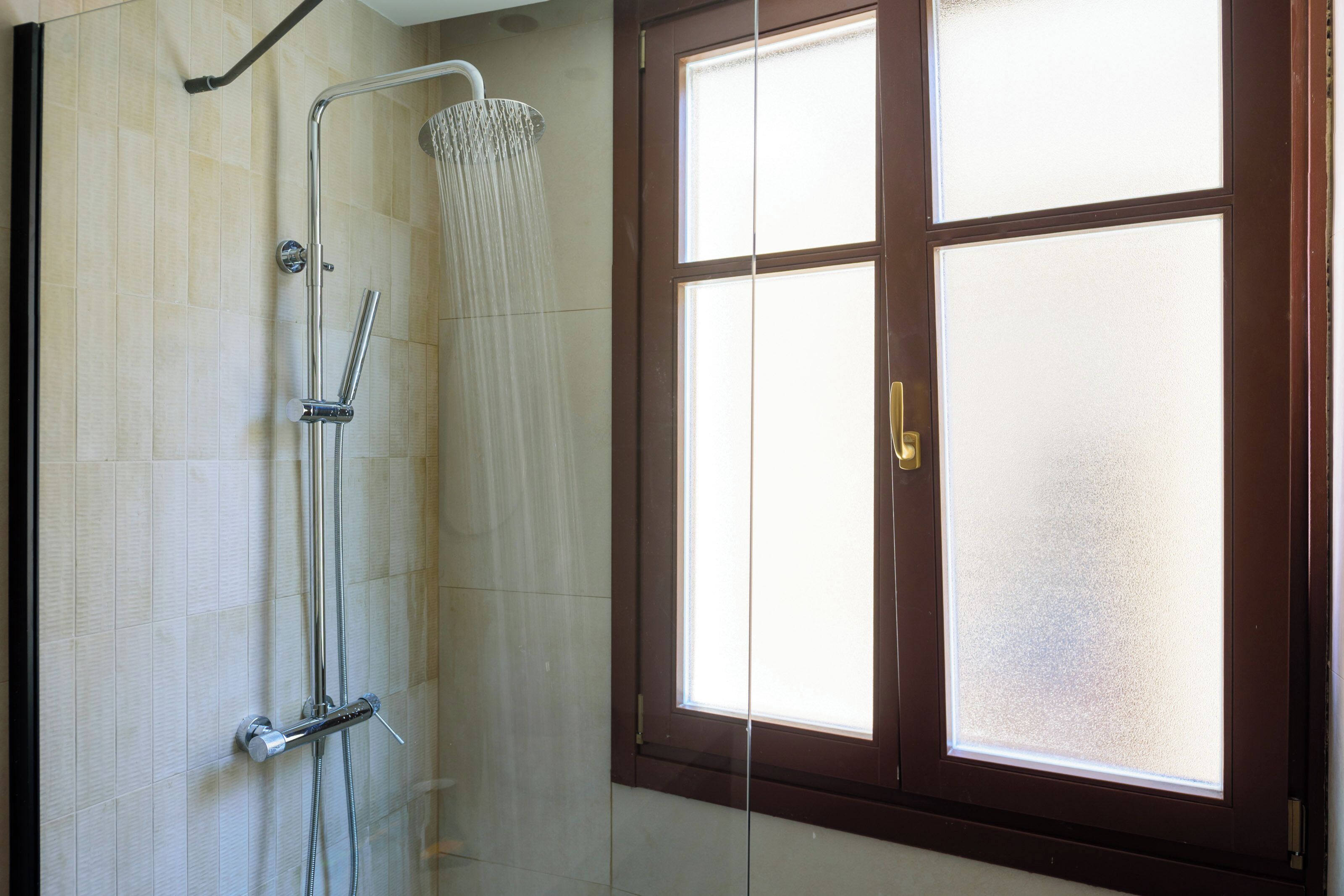 A bathroom with a shower, a window with frosted glass, and a door with a brass handle.