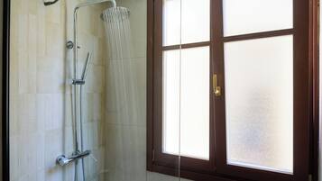 A bathroom with a shower, a window with frosted glass, and a door with a brass handle.