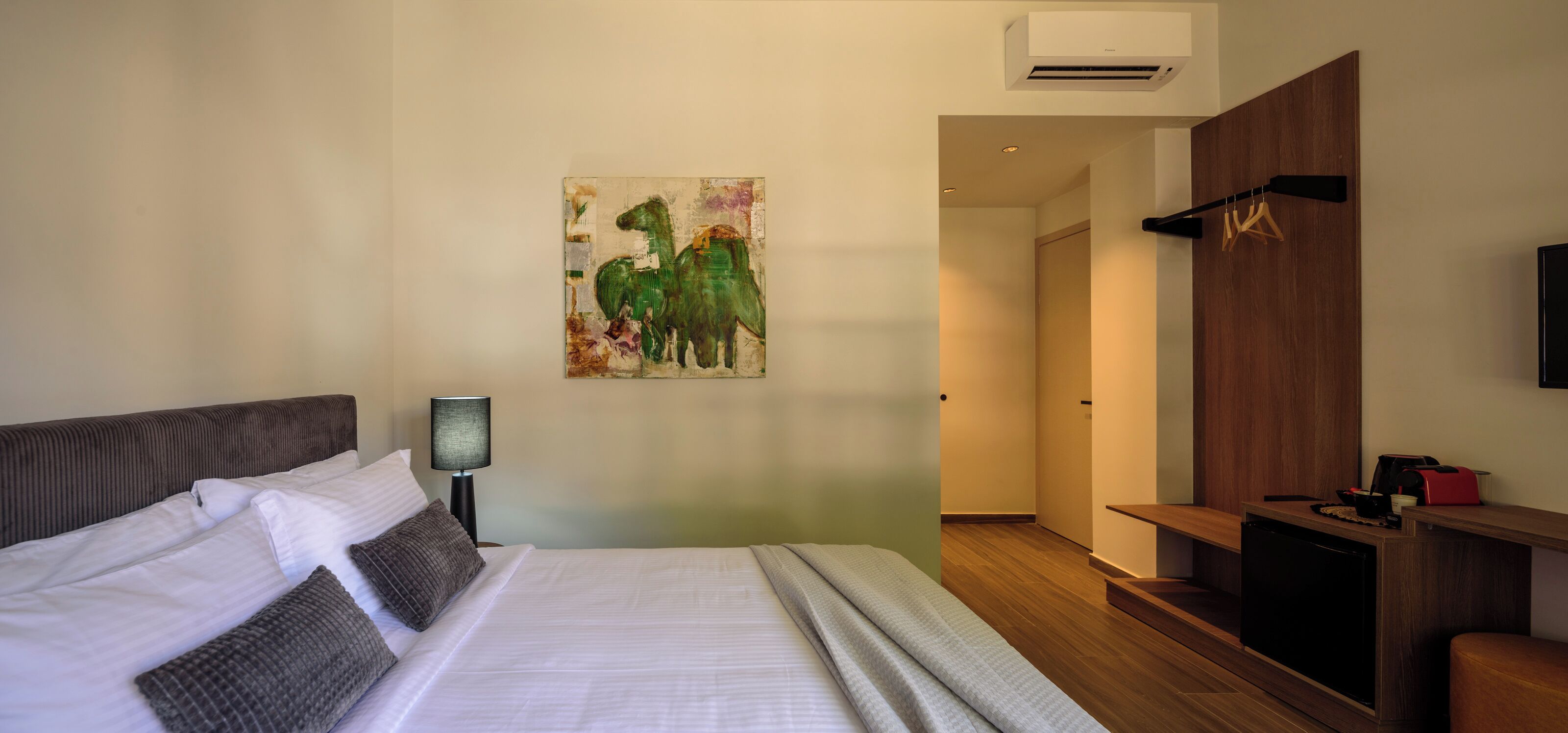 Habitación de hotel con una cama, una lámpara de noche, un cuadro en la pared, un escritorio de madera y un televisor.