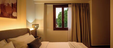 Une chambre d’hôtel avec un lit, une table de chevet avec une lampe, une fenêtre avec des rideaux et un tableau représentant un paysage urbain accroché au mur.