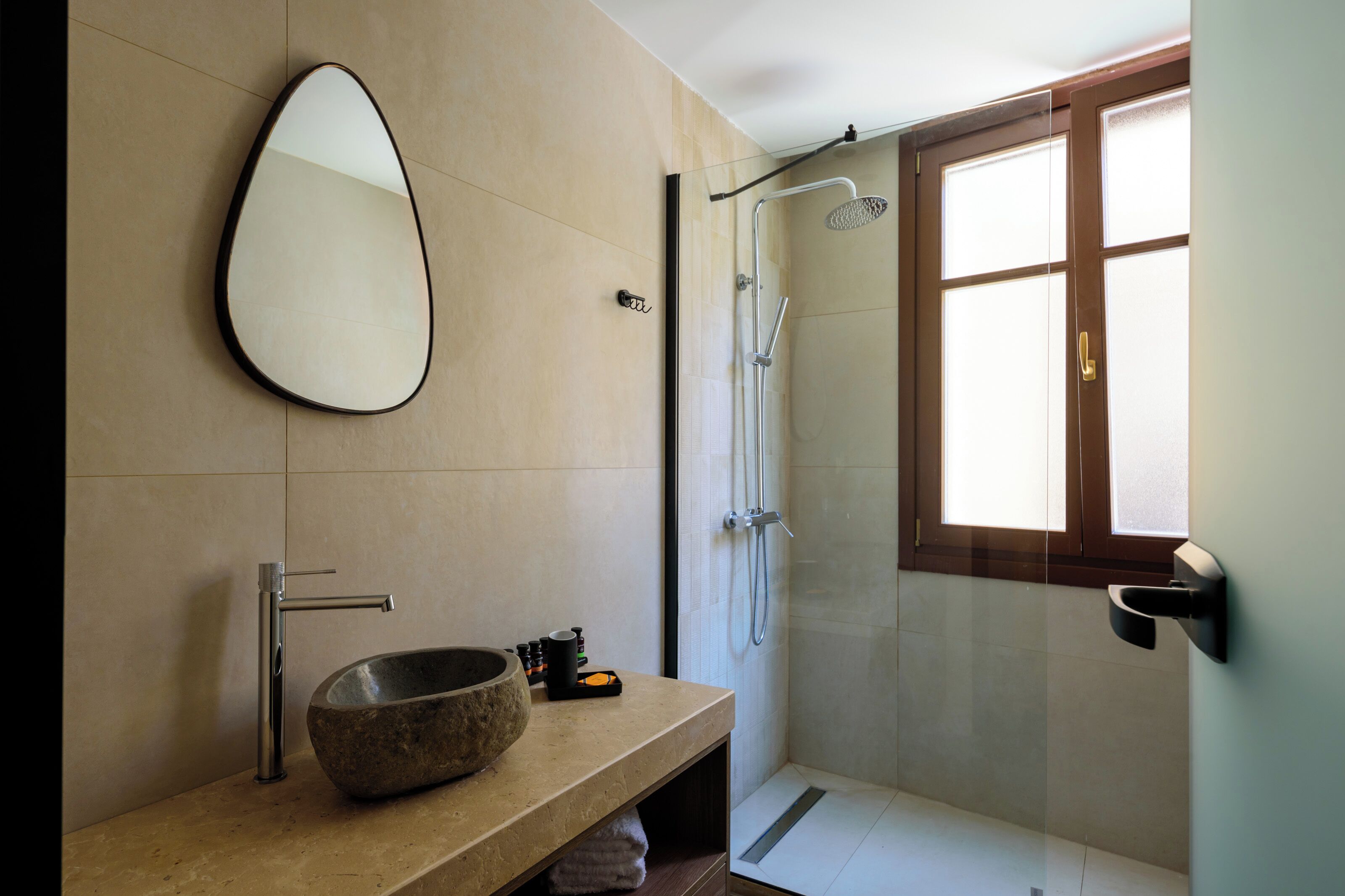 Une salle de bain moderne avec un grand miroir, un lavabo en pierre, une douche et une fenêtre.