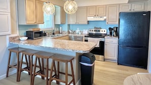 A modern kitchen with granite countertops, stainless steel appliances, wooden bar stools, and pendant lighting. - Spacious 3-bedroom condo steps away from every thing in Ocean City! (Ocean City)