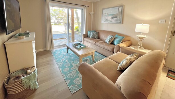 A living room with a sofa, a coffee table, a TV, and a window with curtains. - Spacious 3-bedroom condo steps away from every thing in Ocean City! (Ocean City)