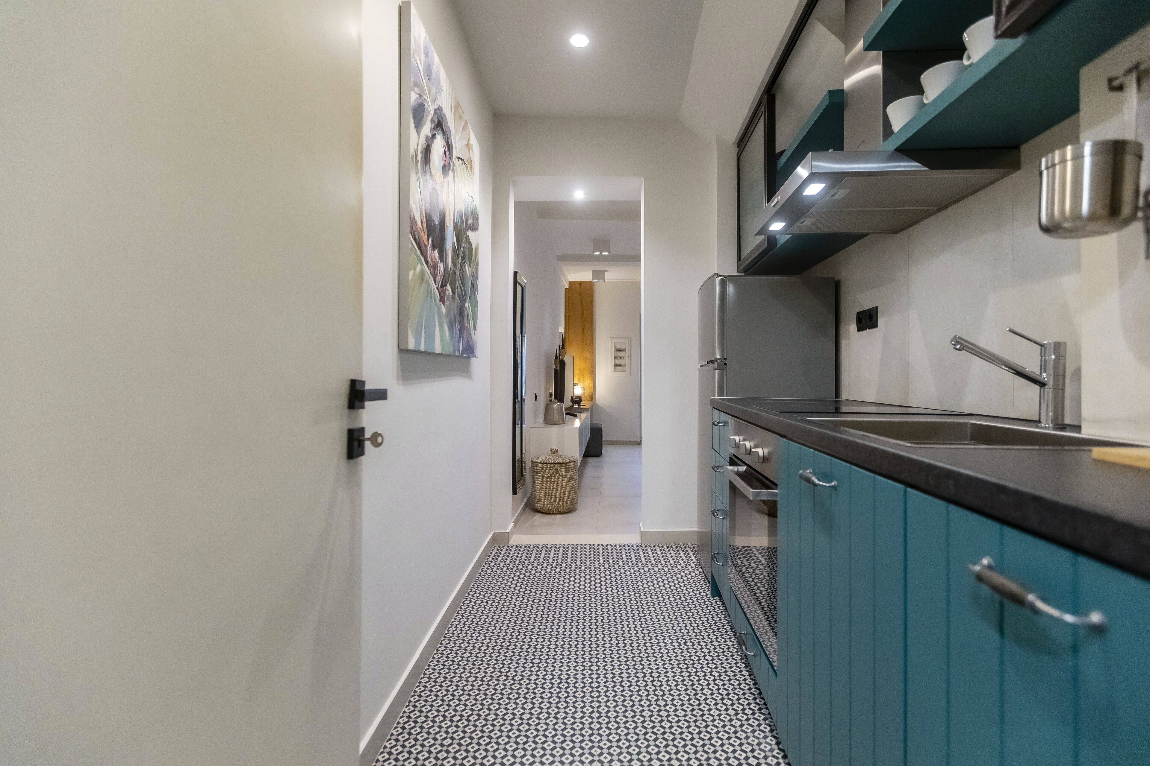 Cocina estrecha con gabinetes color turquesa, pileta de acero inoxidable y piso estampado.