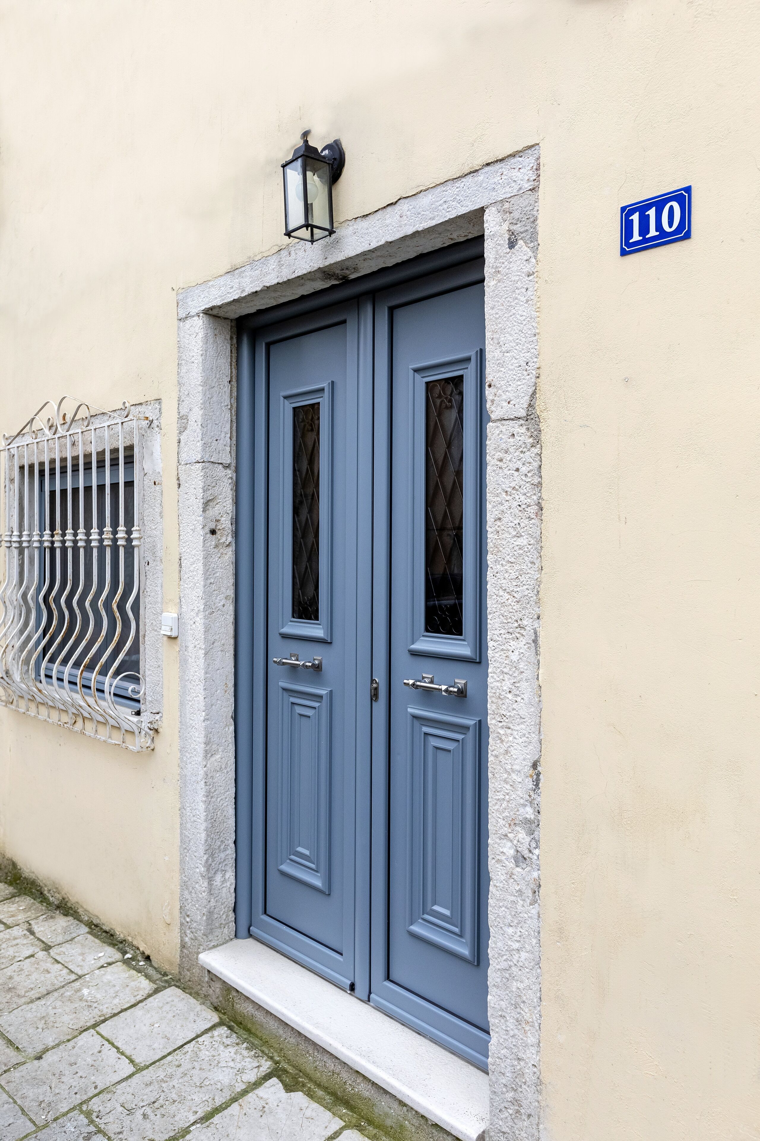 Puerta azul con un cartel con el número 110, una reja metálica y un escalón pequeño que lleva a la entrada.